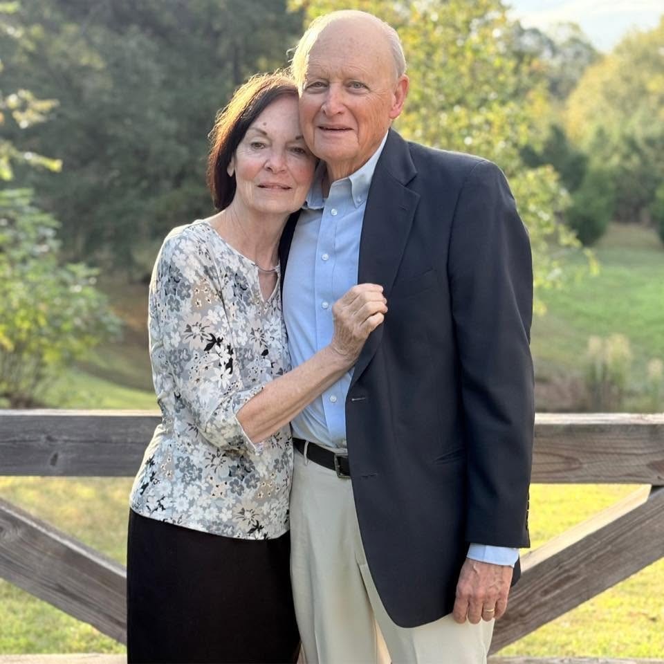 Dr. Ray Conway and his wife standing together by a wooden fence